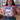 A woman in a pink shirt holds up a spiral-bound book titled 'Dimensions Math Home Instructor's Guide 1B' in front of a classroom background.
